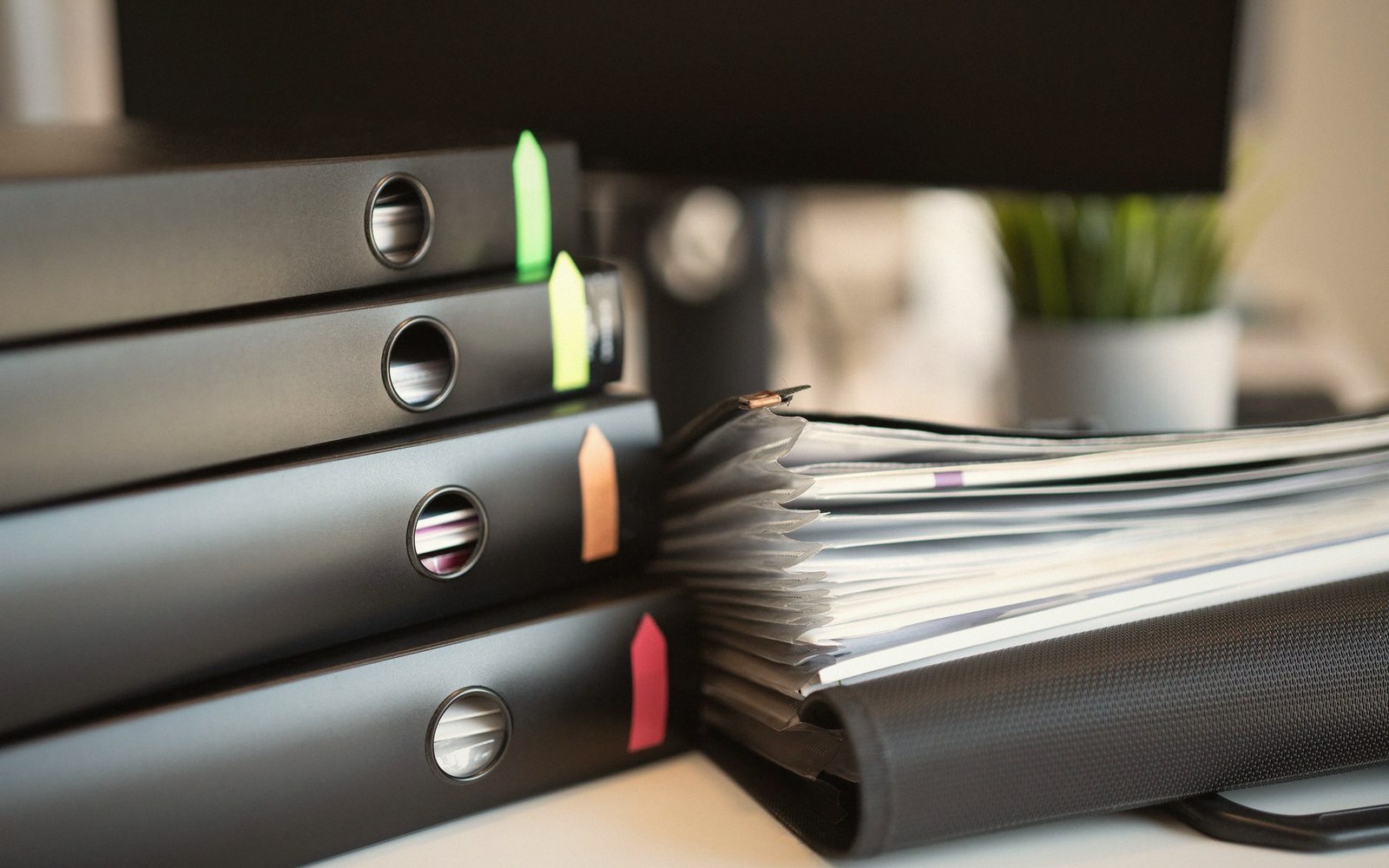 Stack of black ring binders with colored tabs beside an open file of documents on a desk