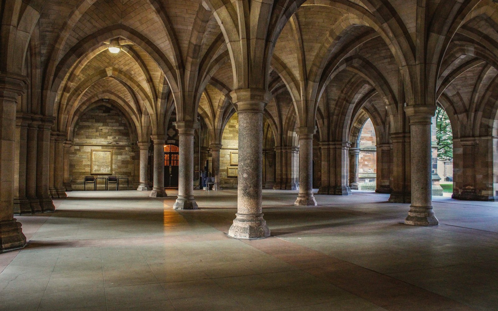 Stone columns and ribbed vaulting form a shadowy Gothic cloister walkway