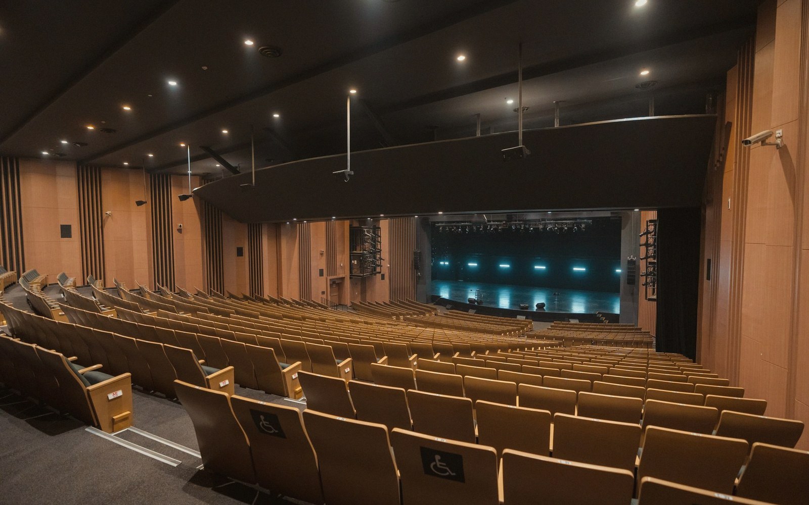 Empty rows of tiered seating face an illuminated stage in a wood-paneled auditorium