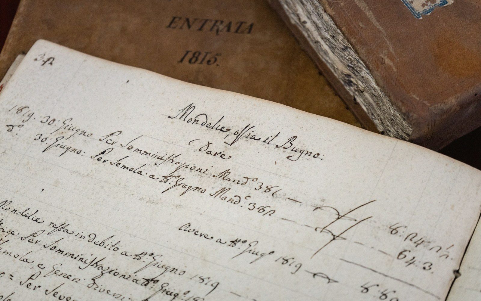 An open handwritten ledger dated 1815 with Italian script and tallied figures, resting on old bound books